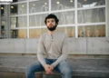 مرد جوانی تیشرت آستین بلند مردانه به رنگ طوی پوشیده با شلوار جین آبی نشسته روی پله